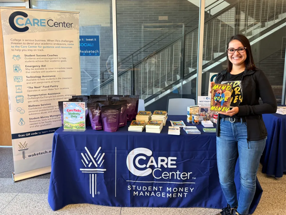 A money management expert shows off a copy of her book in front of a Care Center table stacked with resources.