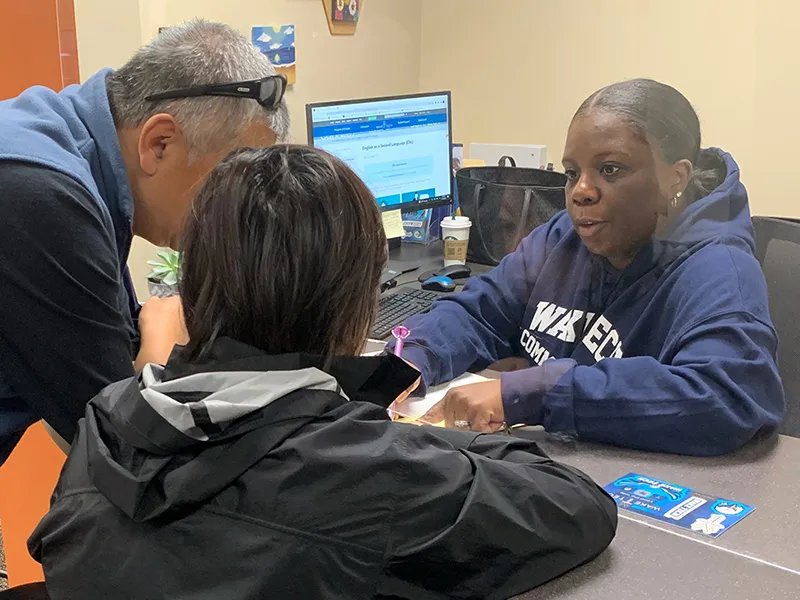 image of two people talking to a woman sitting at a desk wearing a Wake Tech sweatshirt