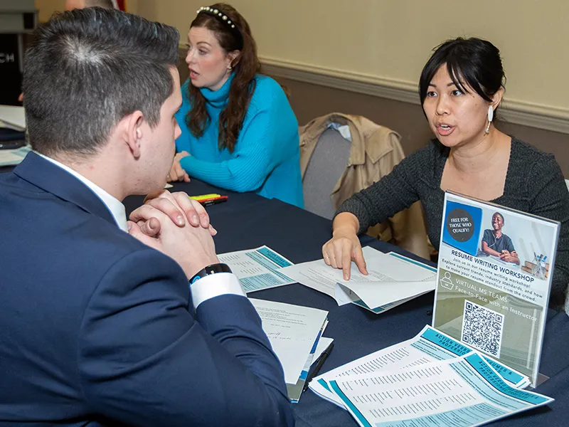 image of a male in a blue suit speaking to a woman sitting at a table