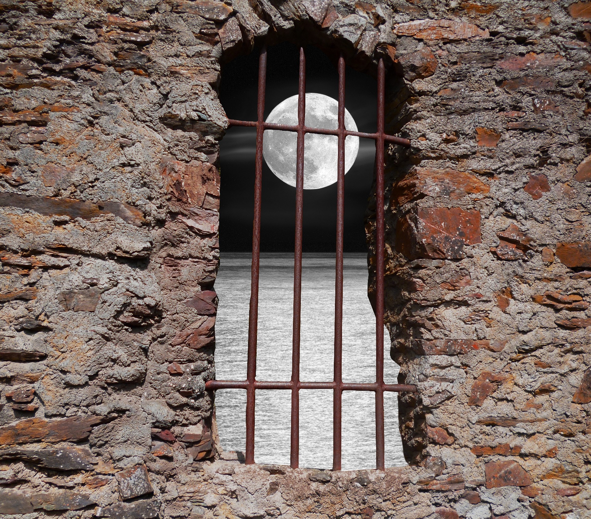 a window in a stone building with iron bars across it and a full moon outside