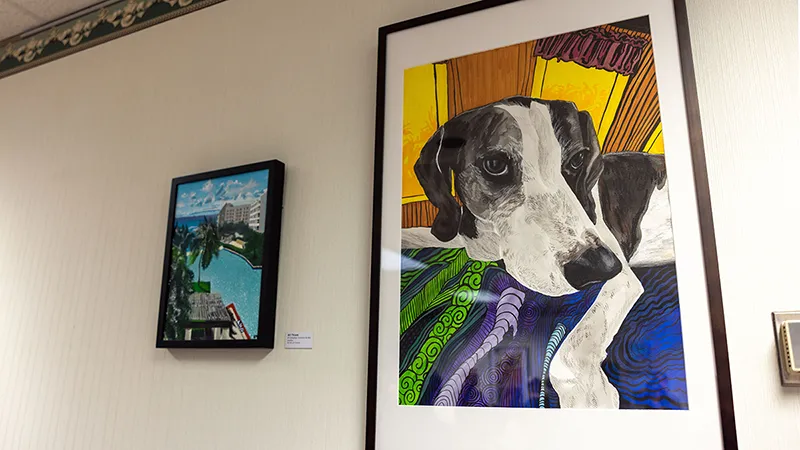 Paintings of a dog and a hotel with a swimming pool and palm trees hanging on a wall