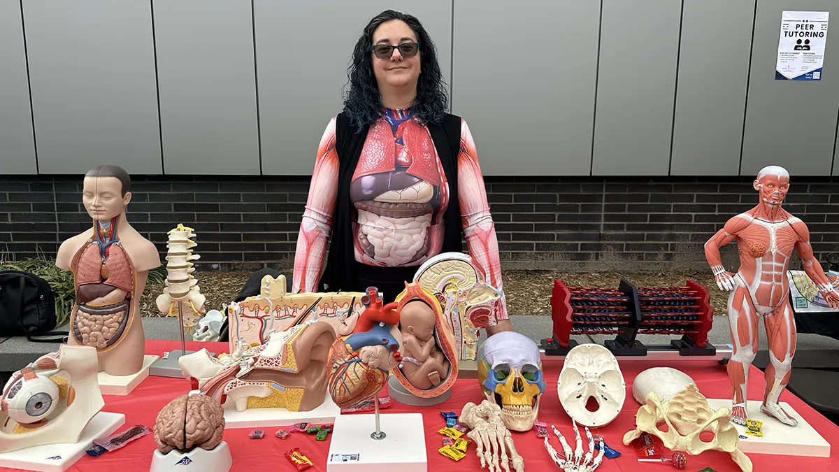 A woman poses behind a table filled with skulls, vertebrae and other depictions of human anatomy for STEM Day.