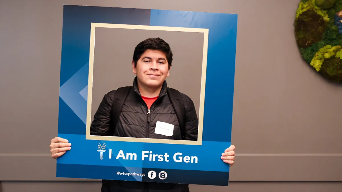 A male Wake Tech student poses for a photo behind an enlarged blue frame with the words "I am first-gen" on it.