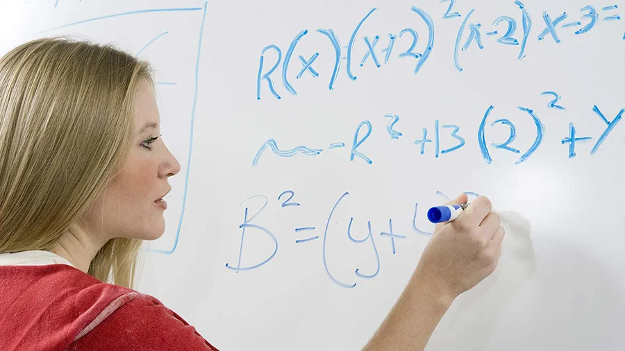 A woman works a math problem on a whiteboard.