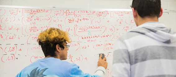 Students work out mathematical problems on a whiteboard.