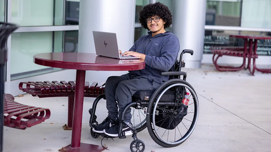 Male student in a wheelchair studying at an outdoor table