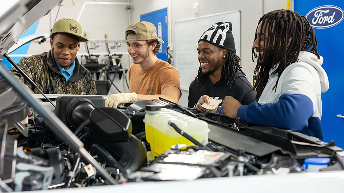 Four Automotive Systems Technology students look under the hood of a vehicle.