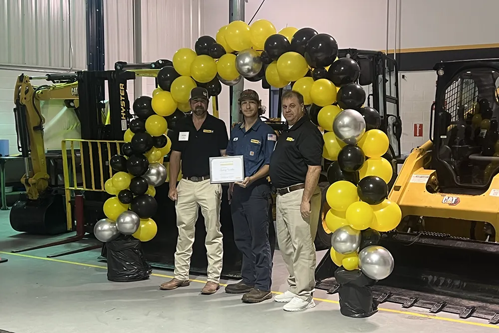 A Wake Tech student poses with instructors in front of a balloon archway after earning a Journeyworker Certificate from the college's apprenticeship program with Gregory Poole Equipment Co.