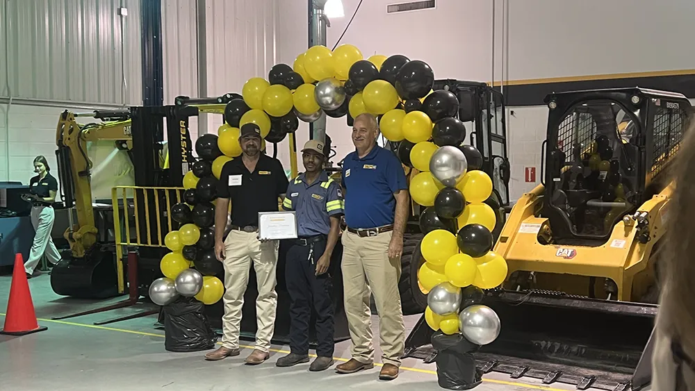 A Wake Tech student poses with instructors in front of a balloon archway after earning a Journeyworker Certificate from the college's apprenticeship program with Gregory Poole Equipment Co.