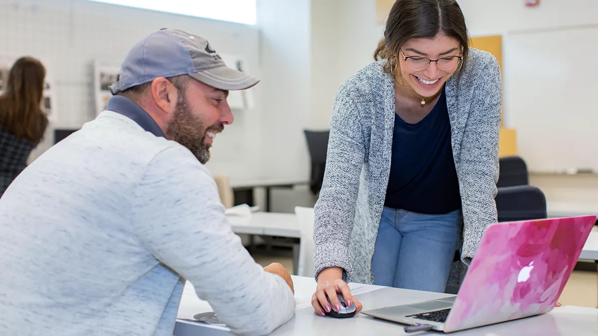Two students work together on a laptop computer.