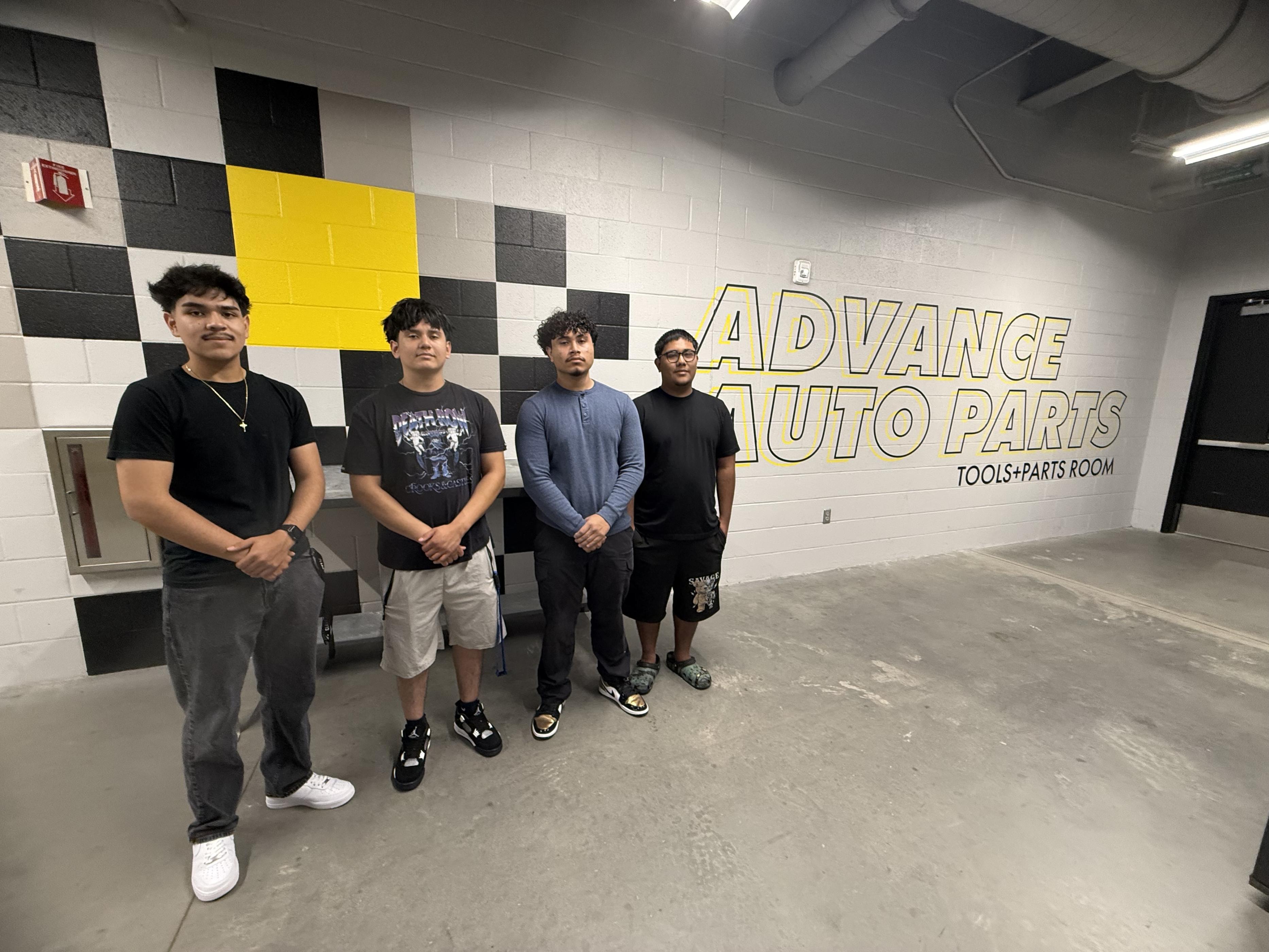 Four future Wake Tech students pose for a photo in front of the Advance Auto Parts logo.