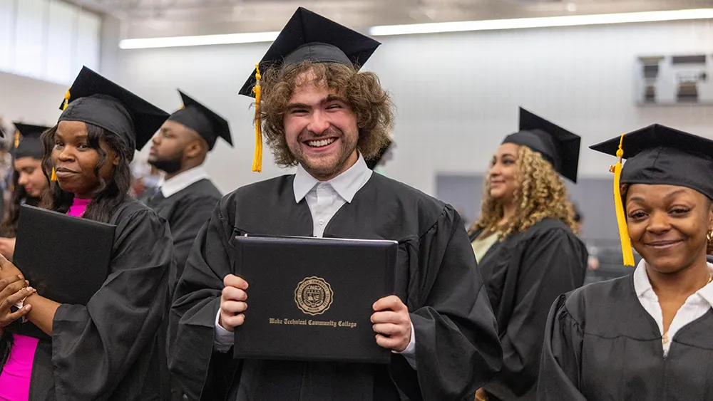 A smiling graduate in cap and gown celebrates after his Wake Tech commencement ceremony.