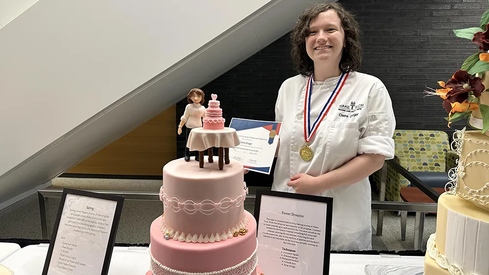 A smiling female student stands next to a pink wedding cake.