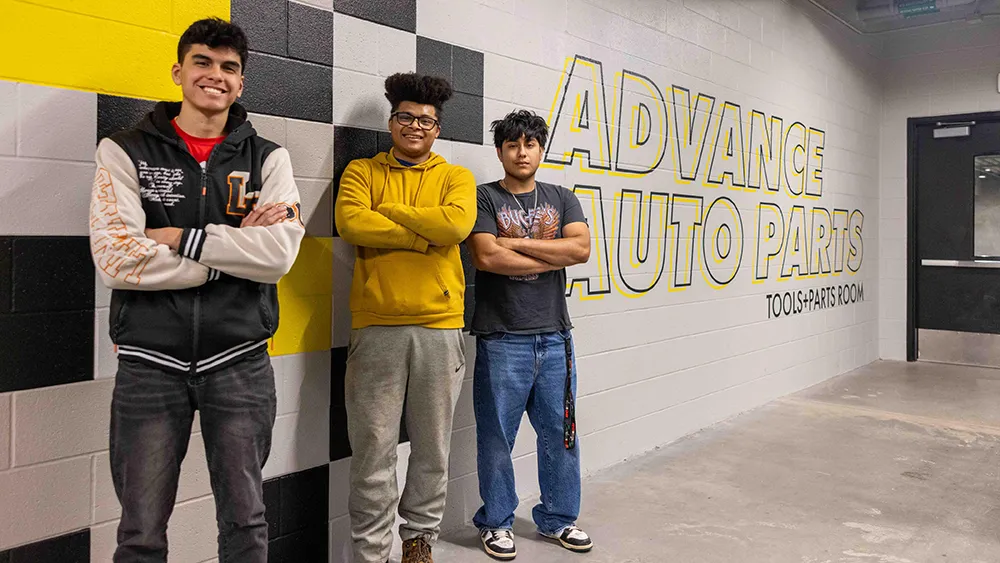 Three recipients of Advance Auto Parts Foundation Future Technicians Scholarships pose for a photo in front of an Advance Auto mural at Wake Tech.