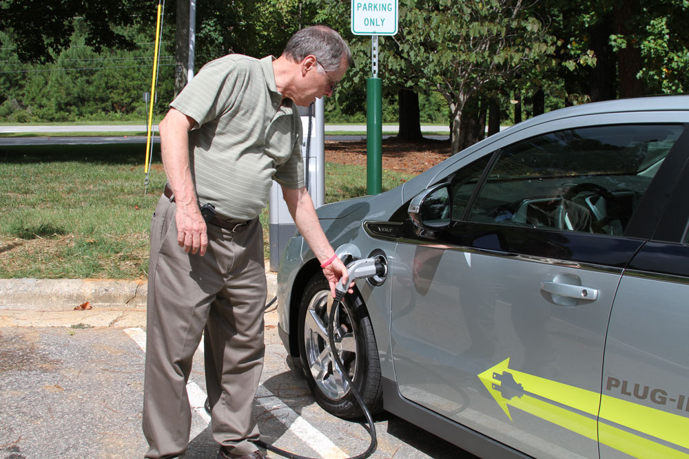 Man plugs electric vehicle into charging station at Wake Tech