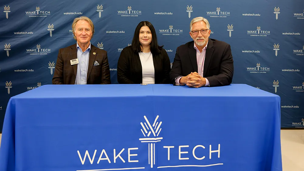 Seated left to right behind a table, Fayetteville Tech President Dr. Mark Sorrells, Sentinel Cybersecurity Bootcamp graduate Jennifer Medina and Wake Tech President Dr. Scott Ralls.