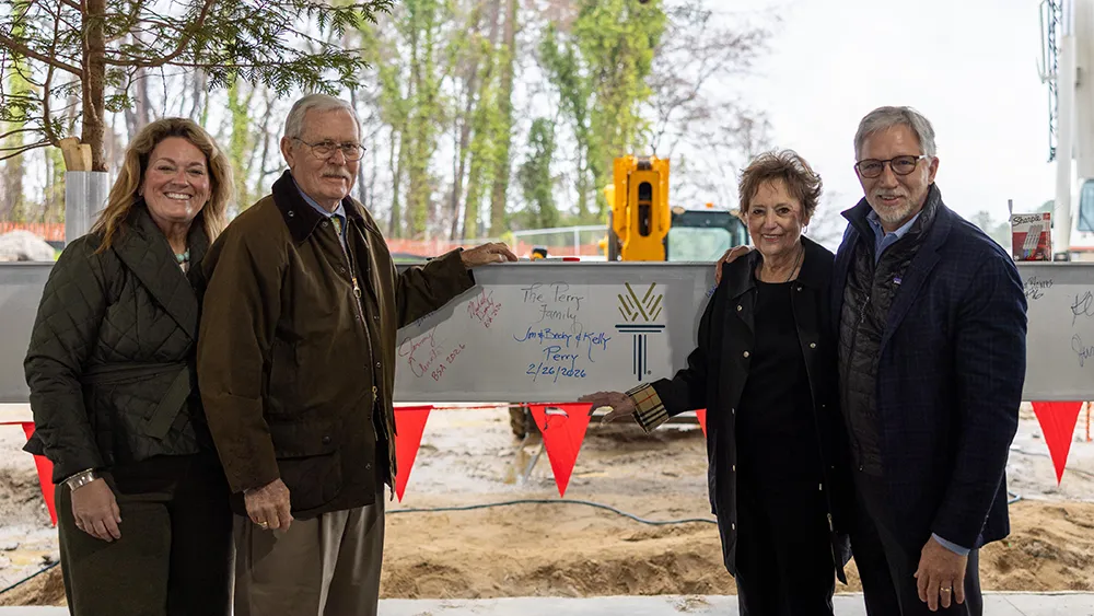 Two men and two women pose next to a steel construction beam.