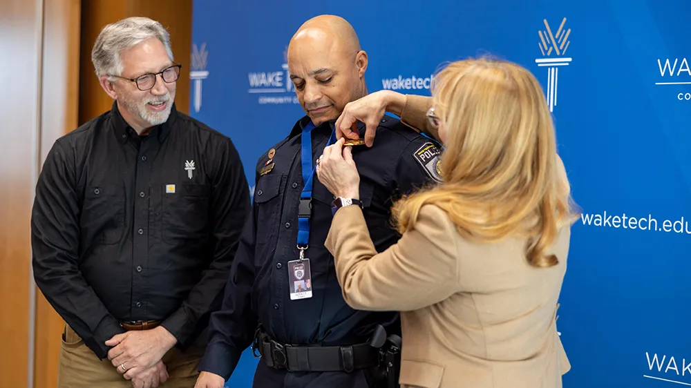 Wake Tech Executive Vice President Dr. Gayle Greene pins a new badge on Police Chief Wyatt Cumbo as college President Dr. Scott Ralls looks on.