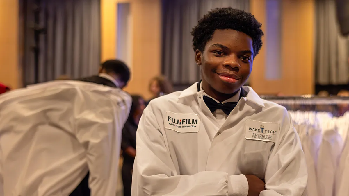 A male biotechnology student wearing a white lab coat poses for a photo.