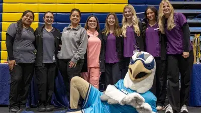 A group seven male and female students in matching blue shirts and windbreakers pose for a photo.