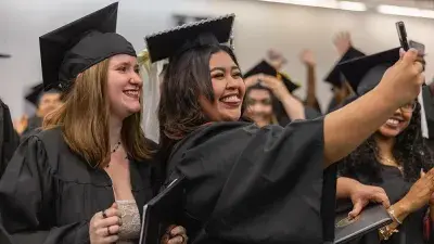 Two graduates in caps and gowns take a selfie after their Wake Tech commencement ceremony.