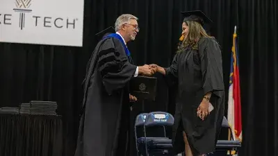 Two graduates in caps and gowns take a selfie after their Wake Tech commencement ceremony.