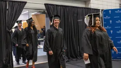 Two graduates in caps and gowns take a selfie after their Wake Tech commencement ceremony.