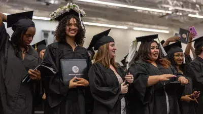 Two graduates in caps and gowns take a selfie after their Wake Tech commencement ceremony.