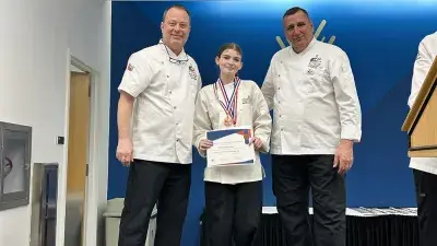 Two men in white chef coats stand next to woman with a medal around his neck holding a certificate.
