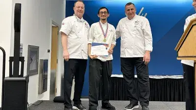 Two men in white chef coats stand next to woman with a medal around his neck holding a certificate.