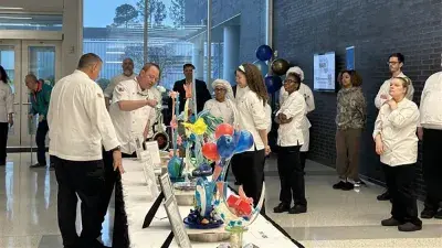 Two men in white chef coats stand next to woman with a medal around his neck holding a certificate.