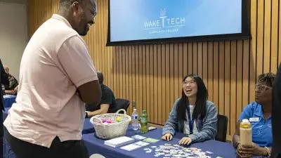 A man makes two Wake Tech staff members seated at a table laugh.
