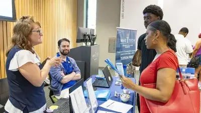 A man makes two Wake Tech staff members seated at a table laugh.