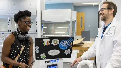 A man makes two Wake Tech staff members seated at a table laugh.