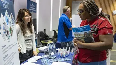 A man makes two Wake Tech staff members seated at a table laugh.