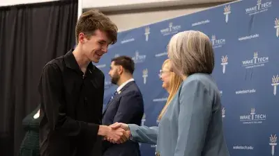 A female Wake Tech student smiles as she processes in at the start of the Phi Theta Kappa honor society induction ceremony.