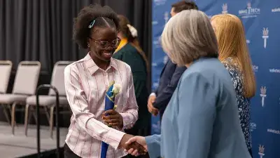 A female Wake Tech student smiles as she processes in at the start of the Phi Theta Kappa honor society induction ceremony.