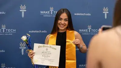 A female Wake Tech student smiles as she processes in at the start of the Phi Theta Kappa honor society induction ceremony.