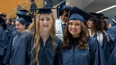 Two Wake Tech students in caps and gowns smile before their graduation ceremony.