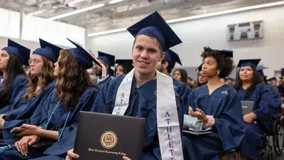 Two Wake Tech students in caps and gowns smile before their graduation ceremony.