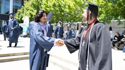 Two Wake Tech students in caps and gowns smile before their graduation ceremony.
