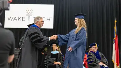 Two Wake Tech students in caps and gowns smile before their graduation ceremony.