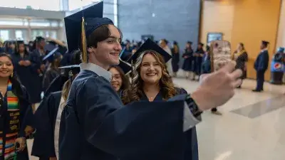 Two Wake Tech students in caps and gowns smile before their graduation ceremony.