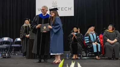 Two Wake Tech students in caps and gowns smile before their graduation ceremony.
