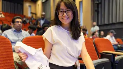 A seated female student holds a white lab coat with a Fujifilm logo on her lap.