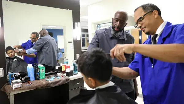 A Wake Tech barbering student cuts a boy's hair as School of Barbering Director William Graham advises him.